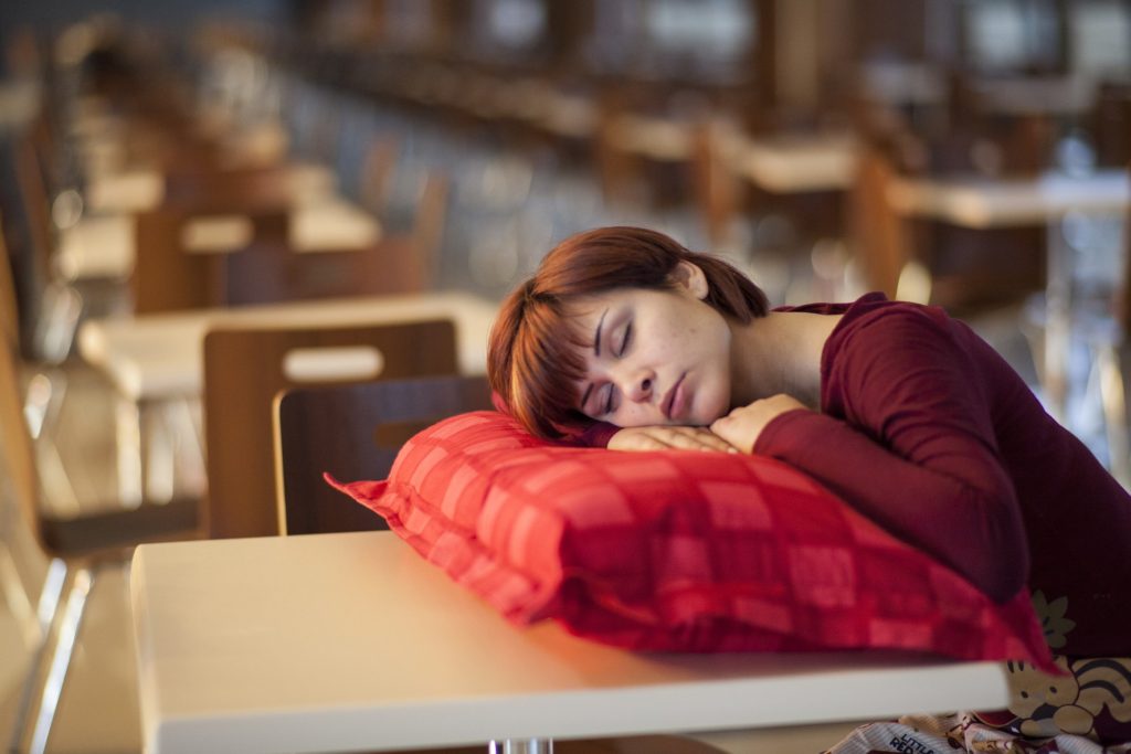 Femme seule endormie sur un oreiller rouge dans une salle de classe