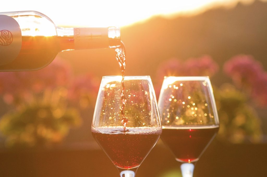 Deux verres de vin rouge servis avec un coucher de soleil en fond.