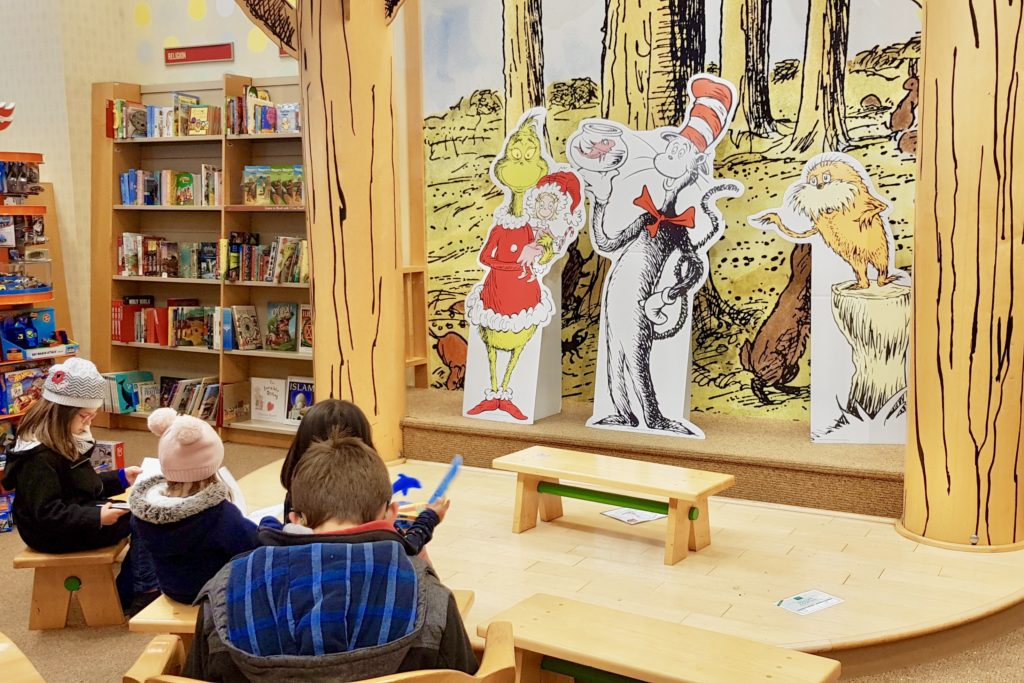 Enfants regardant des livres dans une librairie, assis devant une scène sur laquelle se trouvent des personnages du Dr Seuss